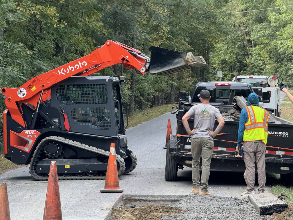 a group of C & R Paving employees loading asphalt into a dump trailer.